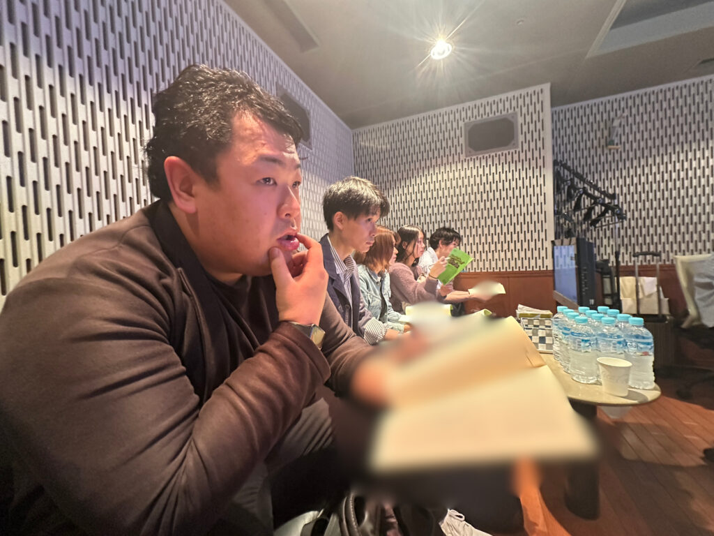収録スタジオ内で音響監督のアドバイス（ディレクション）を真剣な表情で聞く男性声優スクール生