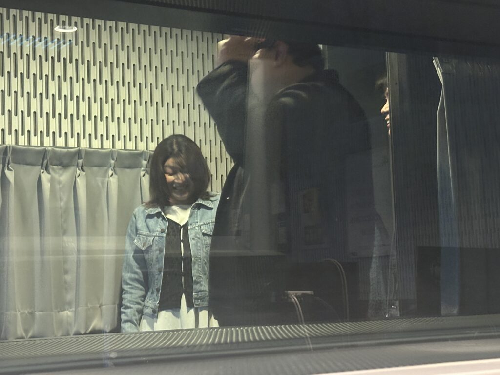スタジオの調整室越しに見える、音響監督のアドバイスを受ける髙松千波さんの収録風景